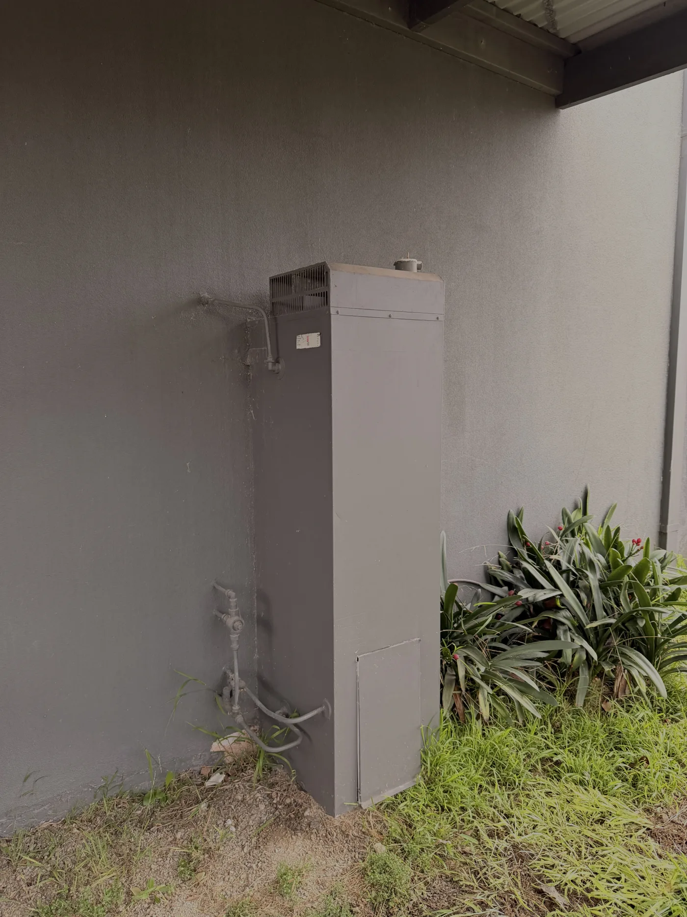 Old electric storage hot water tank on bare ground beside a house